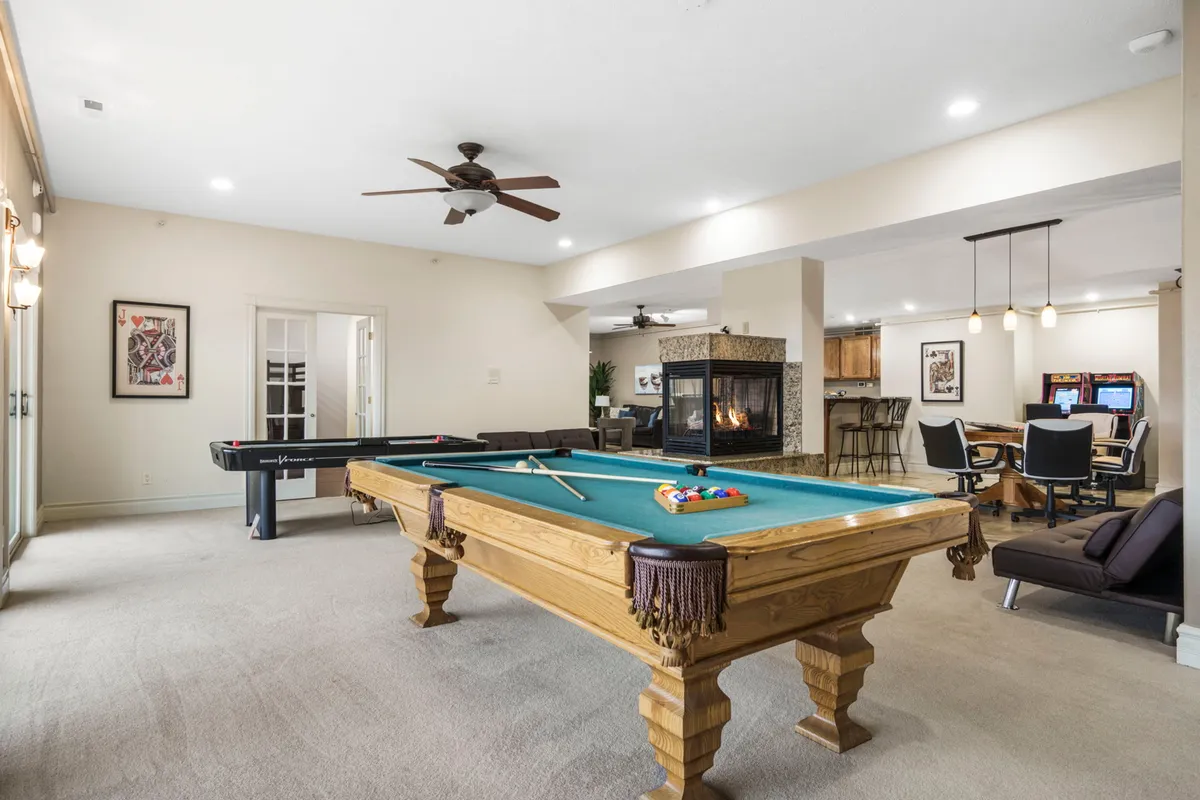 A vibrant game room featuring a pool table as the centerpiece, complemented by a cozy seating area, a warm fireplace, and a game table. The space radiates a casual, welcoming atmosphere ideal for family fun, gatherings, and friendly competition.