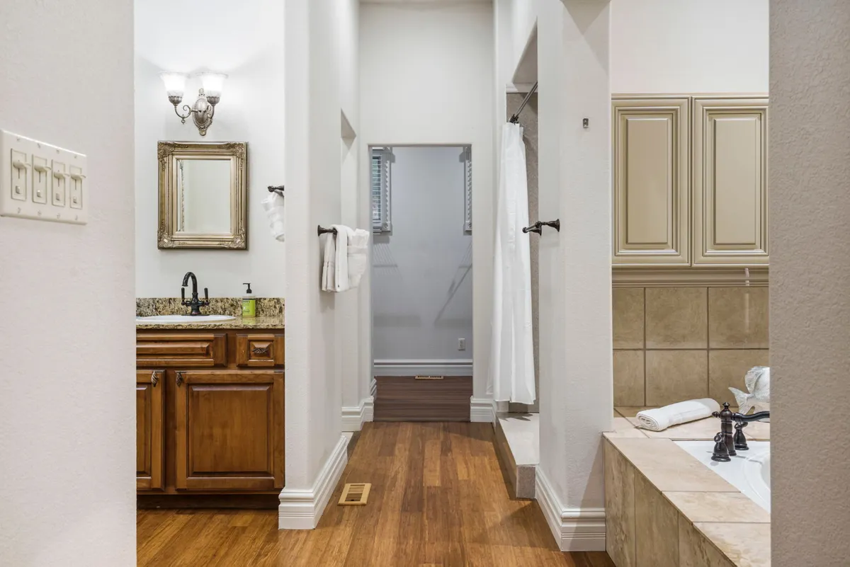 A tranquil bathroom featuring a vanity with a mirror, a soaking bathtub, a separate shower area, and wooden floors. The clean, spa-like atmosphere invites relaxation and showcases the ensuite amenities.