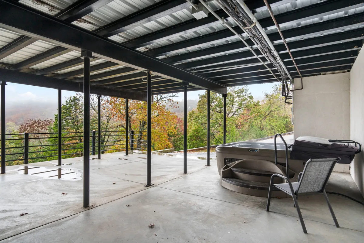 An inviting exterior scene featuring a bubbling hot tub on a deck overlooking lush trees. The metal railing frames the tranquil woodland view, providing a sense of relaxation and connection with nature – ideal after a day exploring Table Rock Lake or nearby Branson attractions.