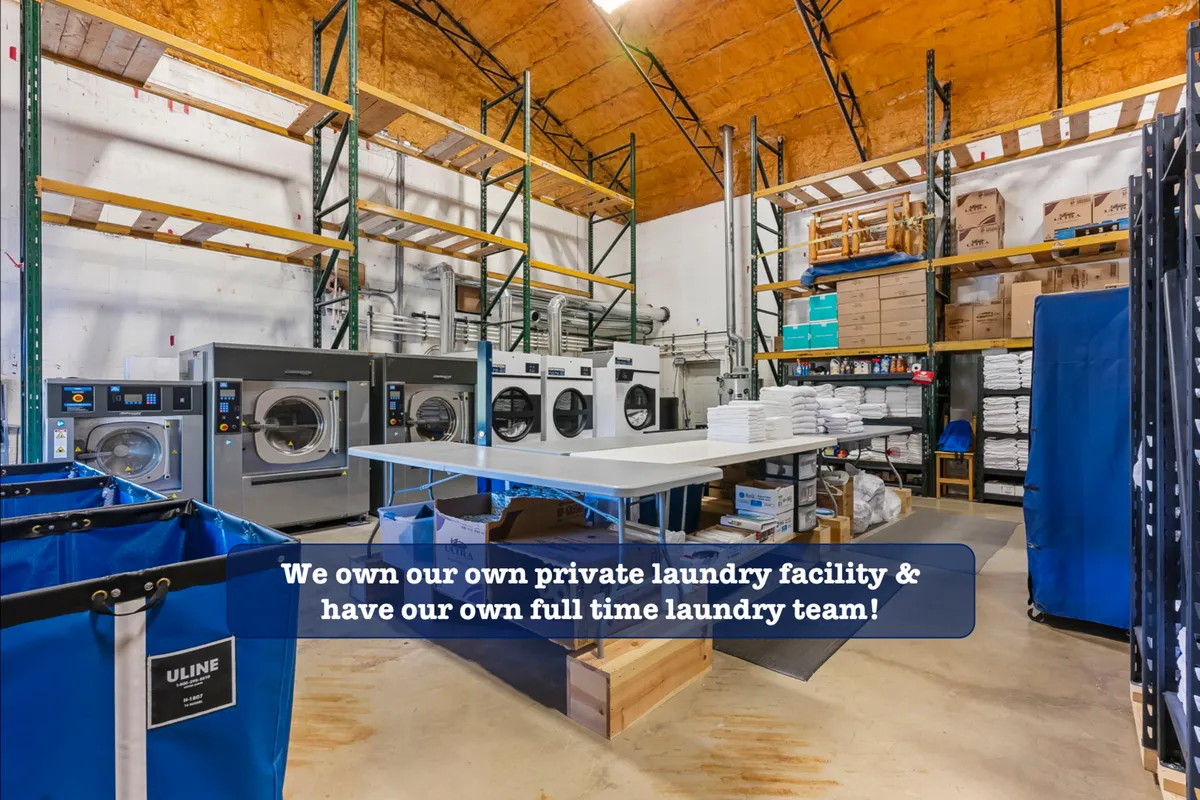 A well-organized laundry area with industrial washing machines, laundry carts, and neatly stacked shelves of supplies. The scene emphasizes cleanliness and the behind-the-scenes attention to detail in linen care.