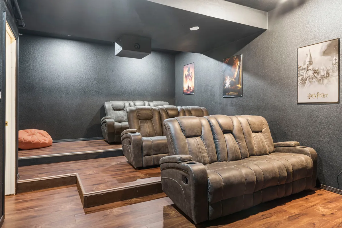 A dedicated theater room with plush seating, movie posters, and a large projection screen. The space is designed for communal experiences and indoor entertainment after a day spent outdoors.