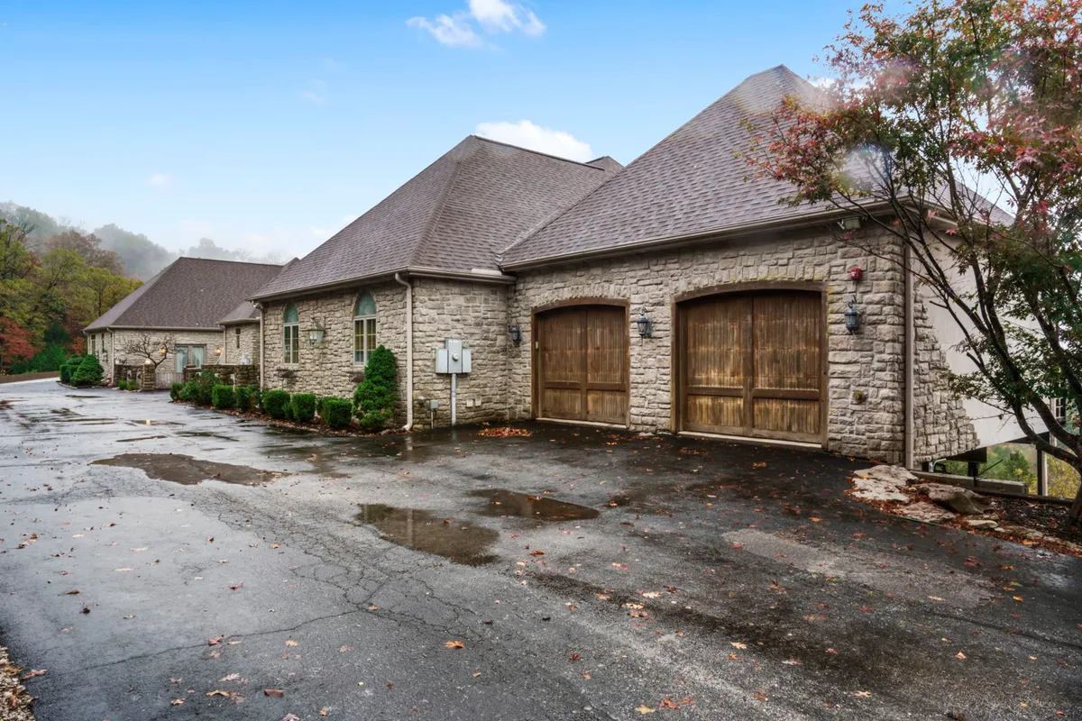 An inviting exterior view of the stone-faced home with wooden garage doors and landscaped greenery. The scene suggests returning from an active day out and hosting gatherings in a welcoming outdoor setting.