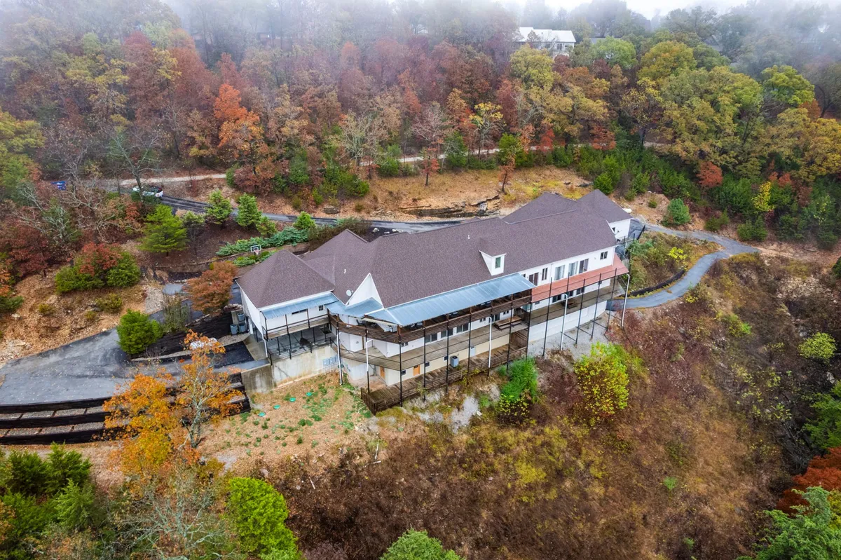 This exterior image features the house nestled within a lush, surrounding forest, with a road leading up to the property. The natural landscape evokes the sense of tranquility and serves as an invitation to explore the outdoor environment, reflecting the proximity to hiking trails and the beauty of the Ozarks.