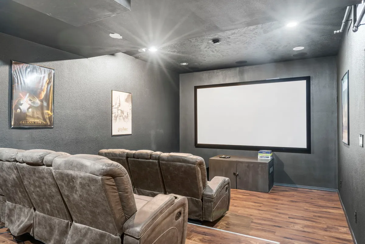 A plush private theater room complete with tiered theater seating, a large projector screen, and movie posters adorning the walls. The environment is immersive, comfortable, and purpose-built for movie nights and cinematic experiences.