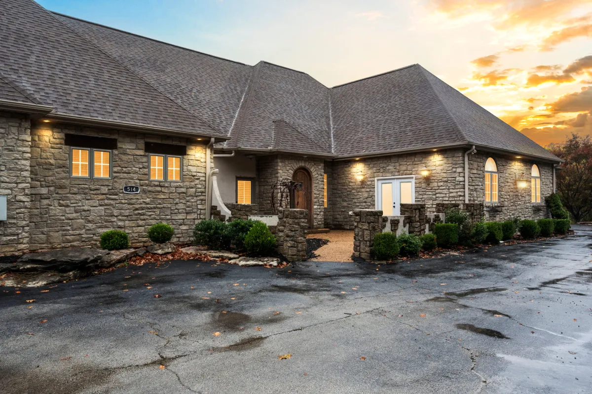 This image features the exterior of Villa Bellissimo, showcasing its impressive stone architecture, large front door, and warmly lit windows. The landscaped bushes and welcoming entry hint at gatherings and festive arrivals.