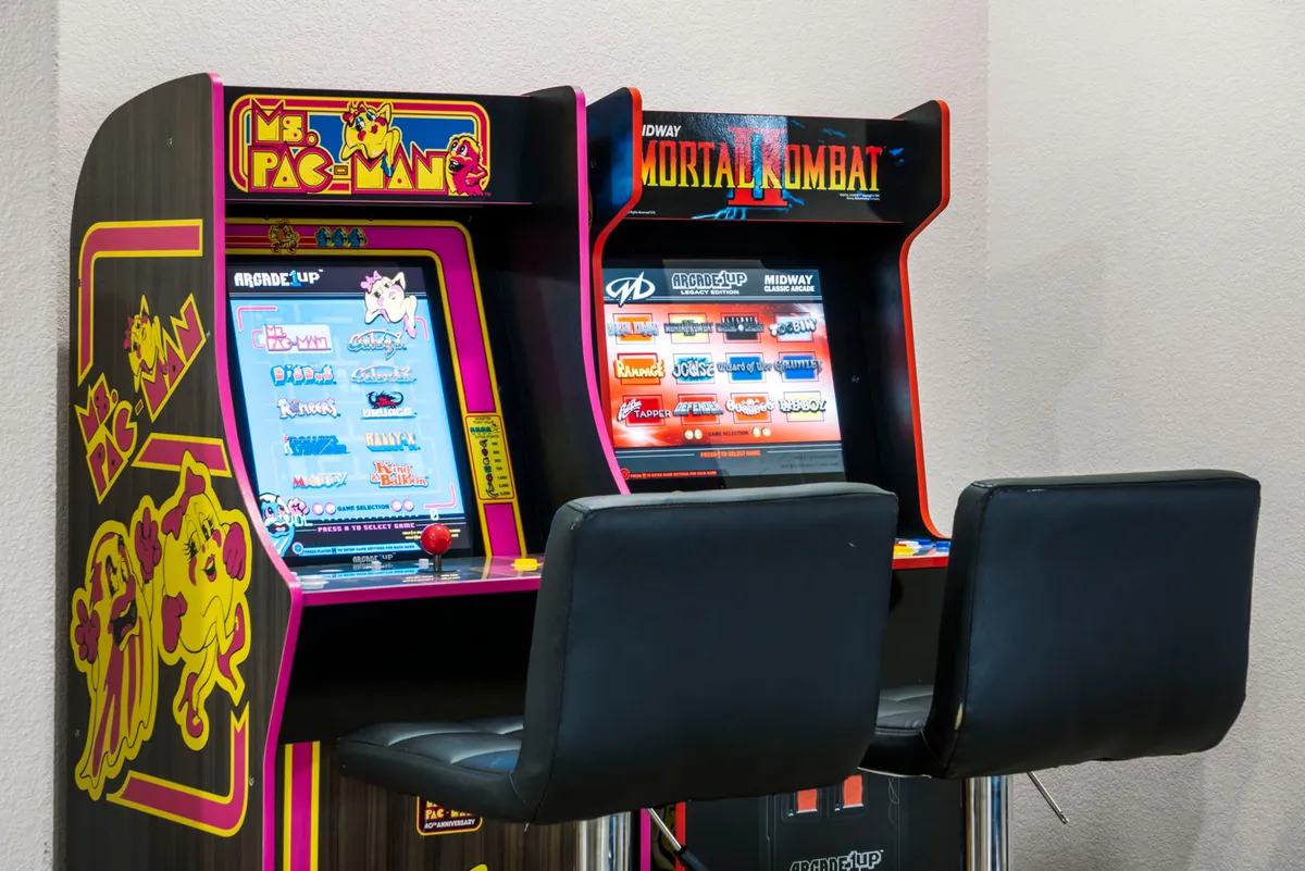 A close-up view of classic arcade machines, including Ms. Pac-Man and Mortal Kombat, inviting guests to relive nostalgic gaming moments. The vibrant machines are set against a backdrop that hints at a lively, playful environment.