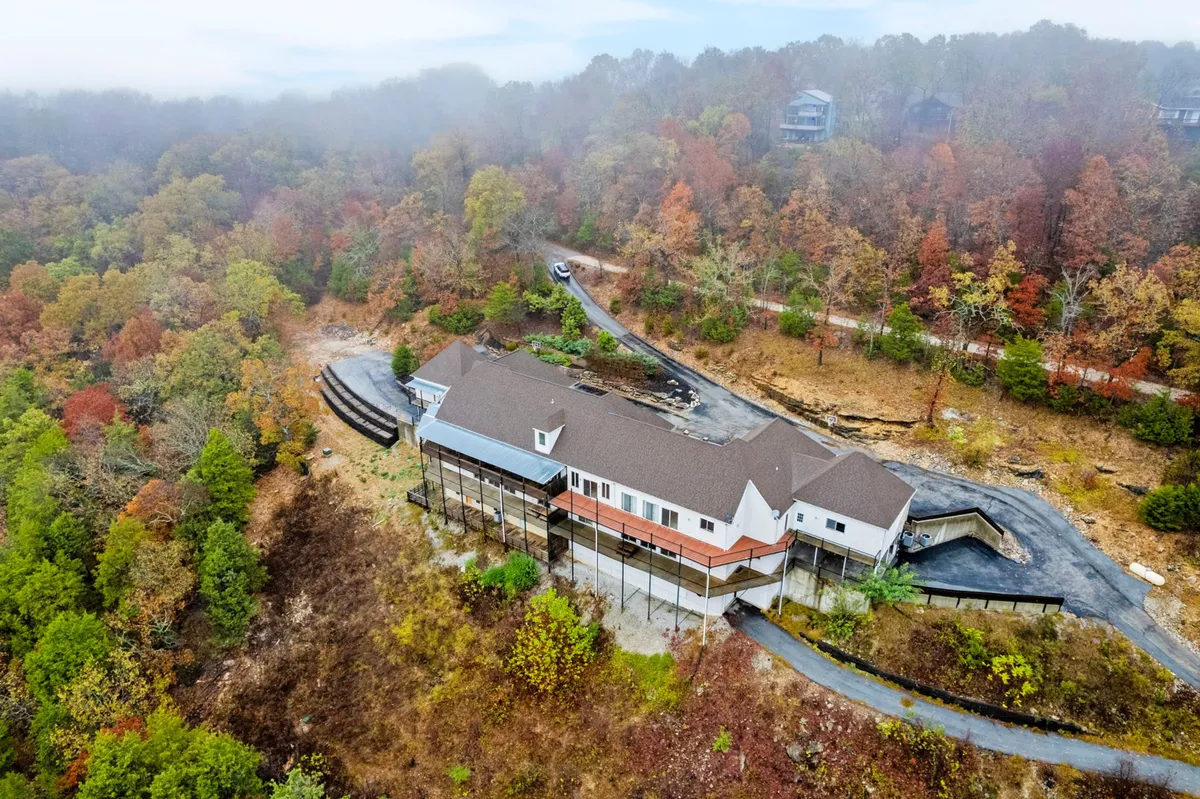 A sweeping exterior shot of the house surrounded by vibrant autumn foliage with a winding driveway. The tranquil setting suggests a peaceful retreat after a day enjoying Branson’s top attractions.