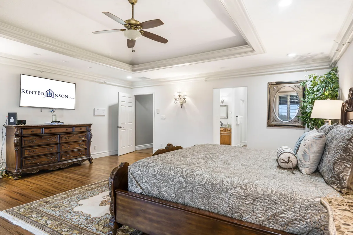 A serene bedroom with a king-sized bed, wooden dresser, wall-mounted television, decorative mirror, and indoor plant. The room exudes comfort, with ample space for guests to relax and enjoy quiet time, and offers a clear view of the room’s smart layout and inviting atmosphere.