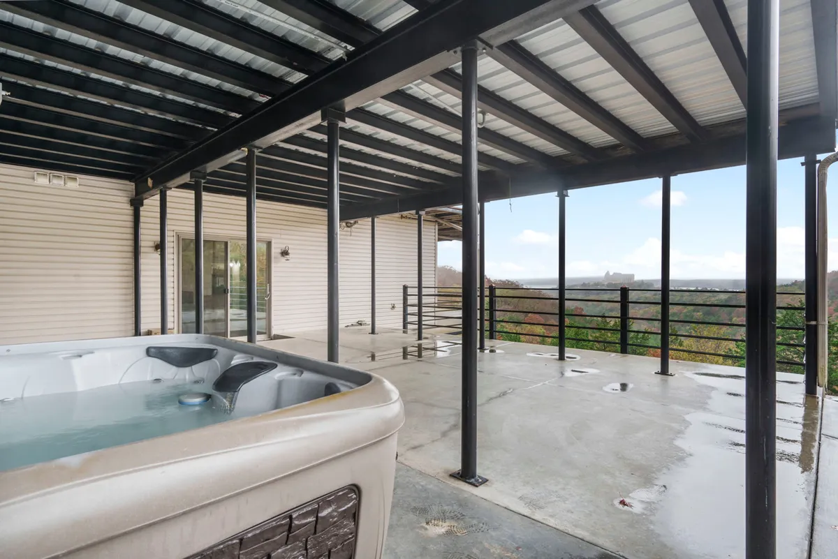 A spacious deck with a private hot tub set beside a wooden railing, overlooking a stunning landscape. The image shows the hot tub as a focal point, with ample space for socializing or relaxing while taking in the expansive views. The natural backdrop creates a serene and inviting environment for unwinding at any hour.